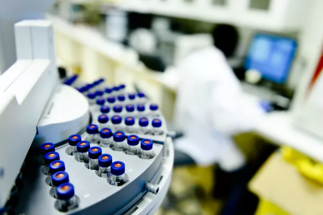 Photo of vials with a researcher at the computer in the background.